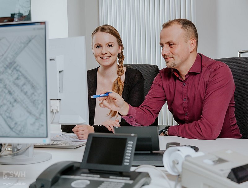 eine Frau und ein Mann unterhalten lächelnd vor dem Bildschirm 