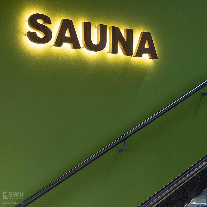 leuchtendes Sauna-Schild an der Wand am Treppenaufgang