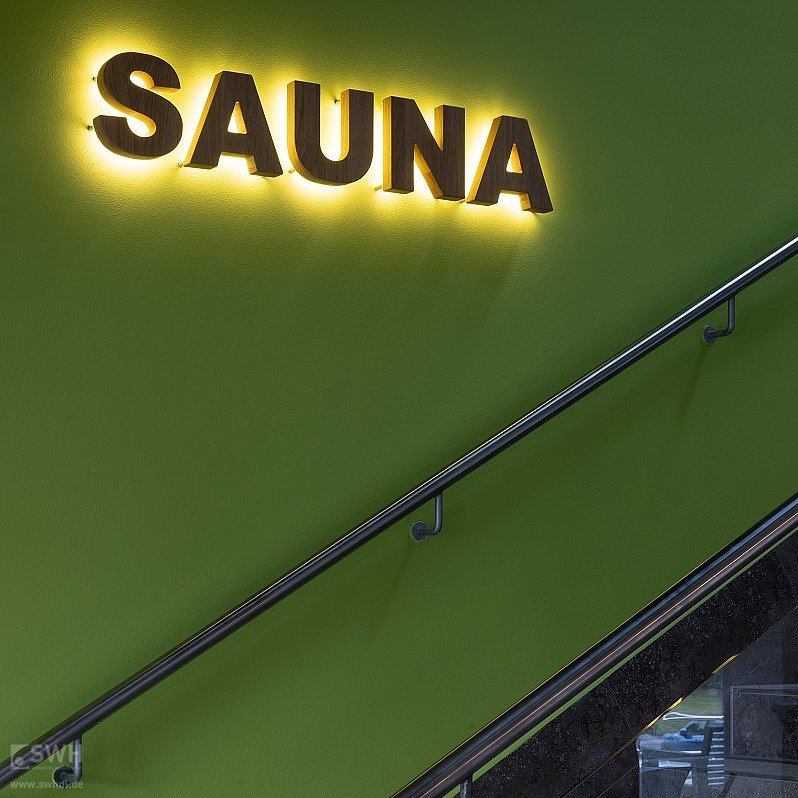 leuchtendes Sauna-Schild an der Wand am Treppenaufgang