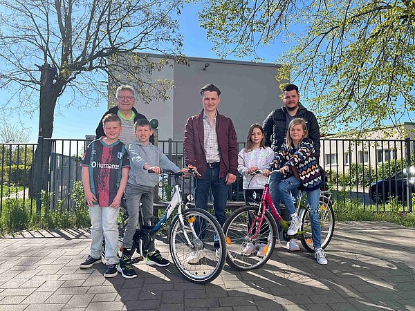 Vincent Ganso, Eisbahnbetreiber steht zusammen mit Herrn Zeymer, Herrn Henning, dem stellvertretenden Schulleiter und 4 Schüler:innen mit 2 Fahrrädern auf dem Schulhof der Erich-Kästner Grundschule
