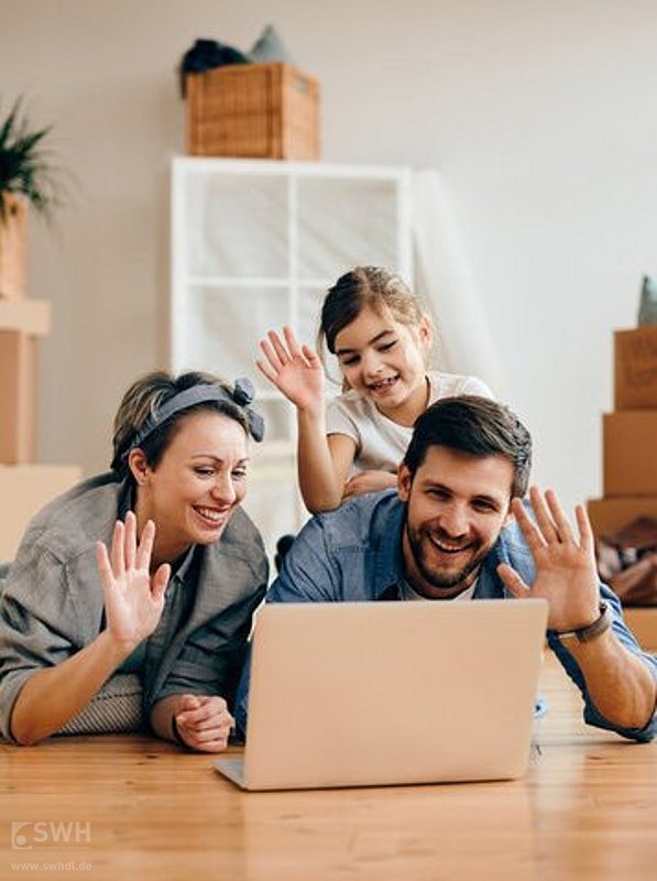 junge Familie auf dem Boden liegend vor dem Laptop in neuer Wohnung umgeben von Umzugskartons